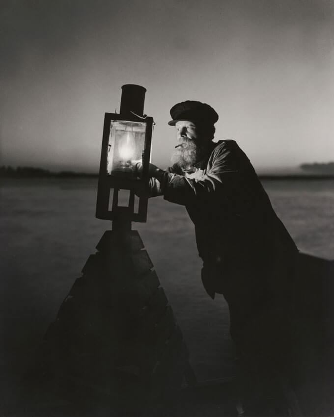 A black and white photo of a person lighting a lantern on top of a buoy.