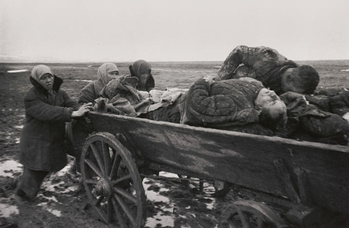 Black and white photograph of three people pushing a cart loaded with casualties.