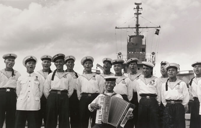 Group of sailors on a ship's deck, with one playing an accordion.
