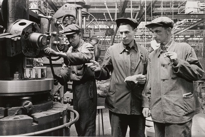 Three people stand in front of a machine in an industrial setting.