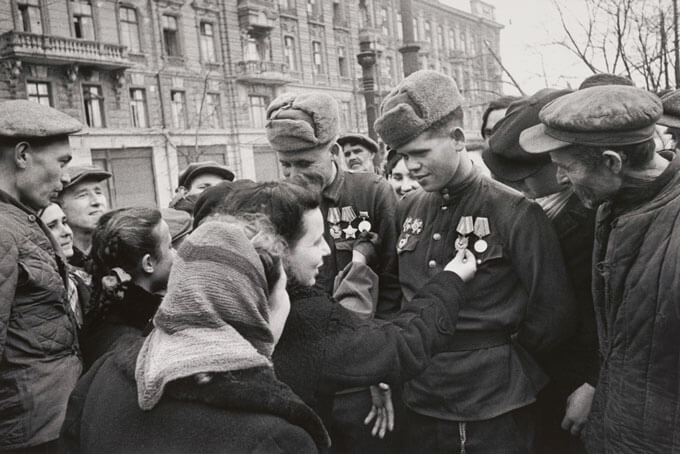 Soldiers with medals surrounded by a crowd in a city setting.