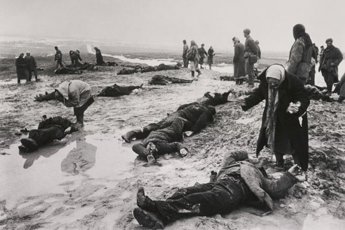 Black and white photo of civilians grieving over the bodies of casulaties in the war.