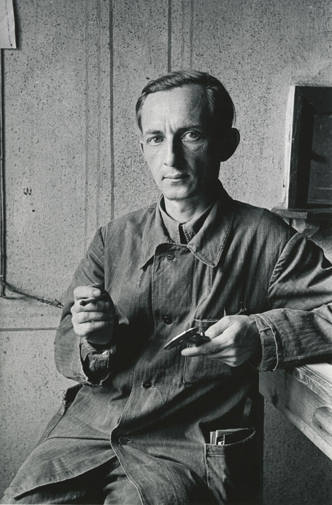 A black and white photo of a person holding a cigarette in one hand and calipers in the other.
