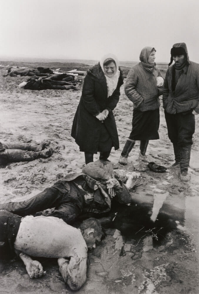 Black and white photo of three people mourning war casualties on the ground around them.