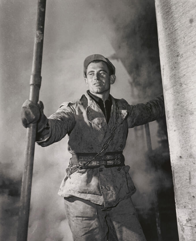 A black and white photo of a person in a uniform holding a post in an industrial setting.