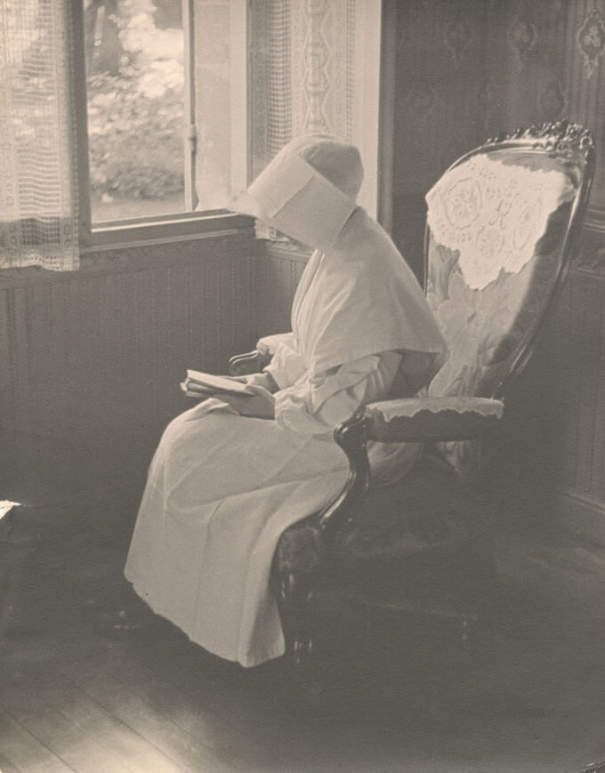 A nun sits in a chair reading a book.