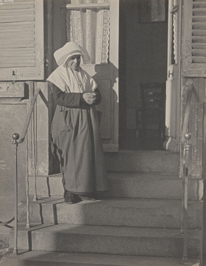 A nun stands on the front steps of a building.