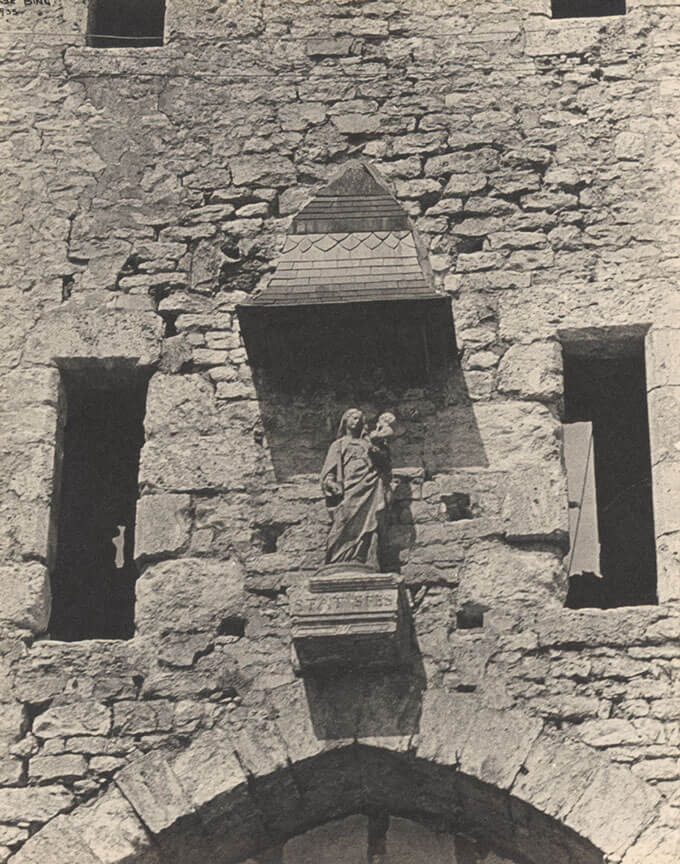 A statue sits in the stone above a stone archway.