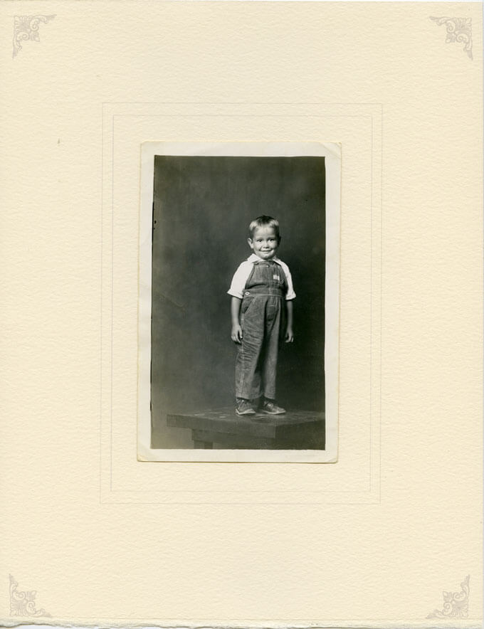 Boy in overalls standing on table, ca. 1940