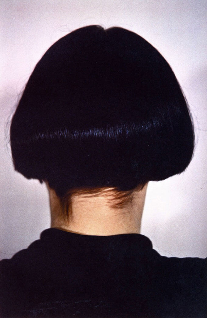 Tightly cropped portrait of a person facing away from viewer with bobbed black hair wearing a black shirt