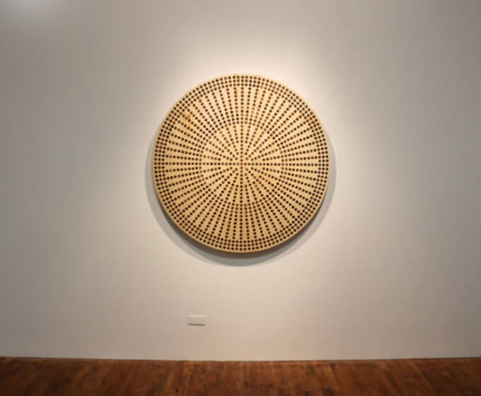 Flat wooden circle with a pattern of concentric circles made of evenly spaced pennies embedded in the wooden surface