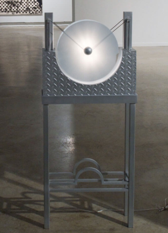 A metallic sculpture with a circular frosted disc on a diamond-patterned metal stand.  