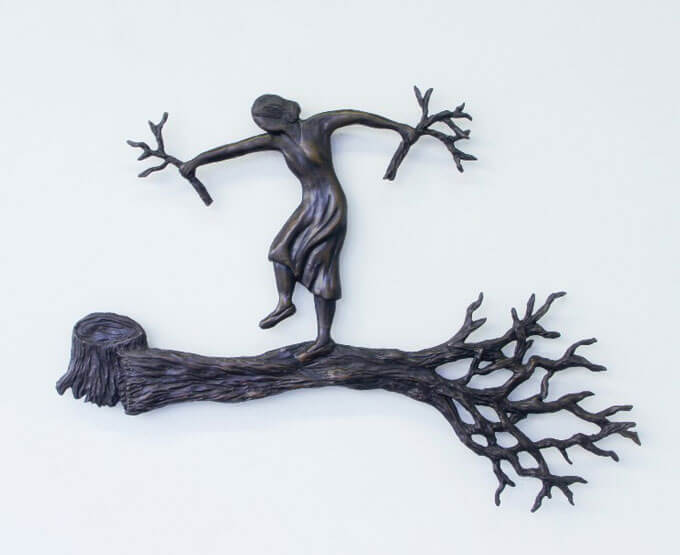 Bronze sculpture of a person balancing on a tree branch with extended arms holding thin branches.