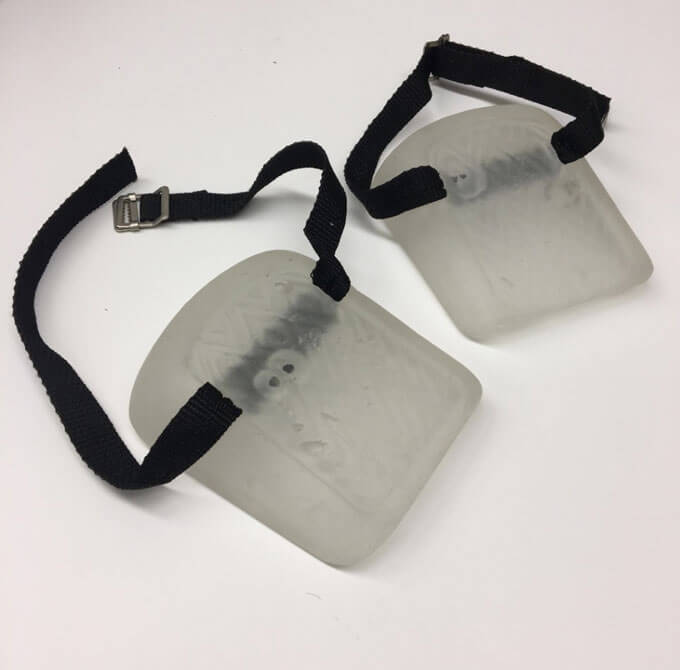 A pair of translucent knee pads with black straps and metal buckles on a white surface.