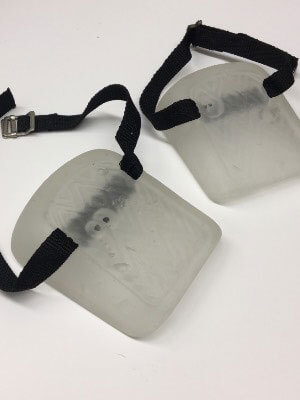 A pair of translucent knee pads with black straps and metal buckles on a white surface.