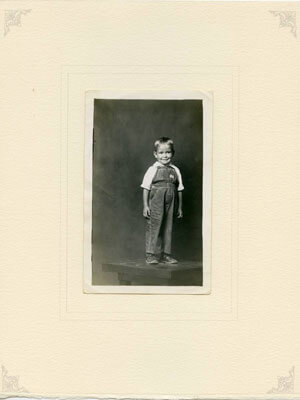 Boy in overalls standing on table, ca. 1940