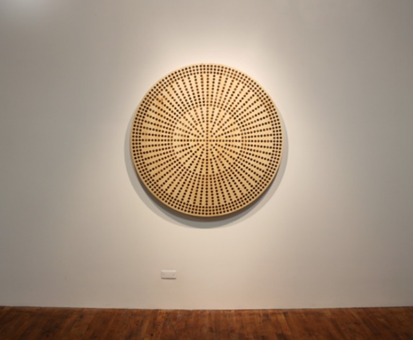 Flat wooden circle with a pattern of concentric circles made of evenly spaced pennies embedded in the wooden surface 